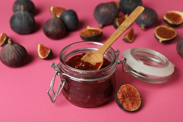 Jar with fig jam and spoon, and ingredients on pink background