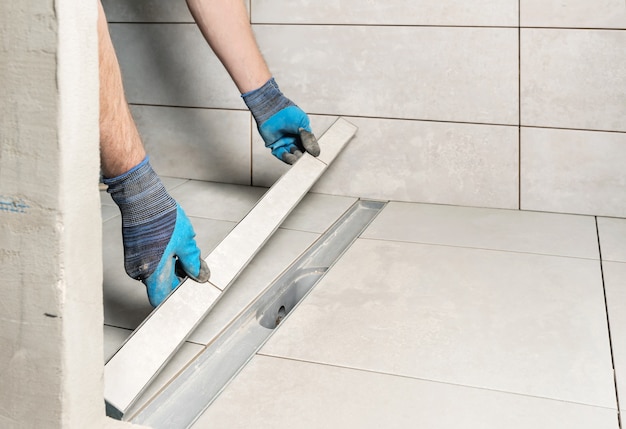 A worker is installing a drain lid decorated with ceramic tiles in the bathroom