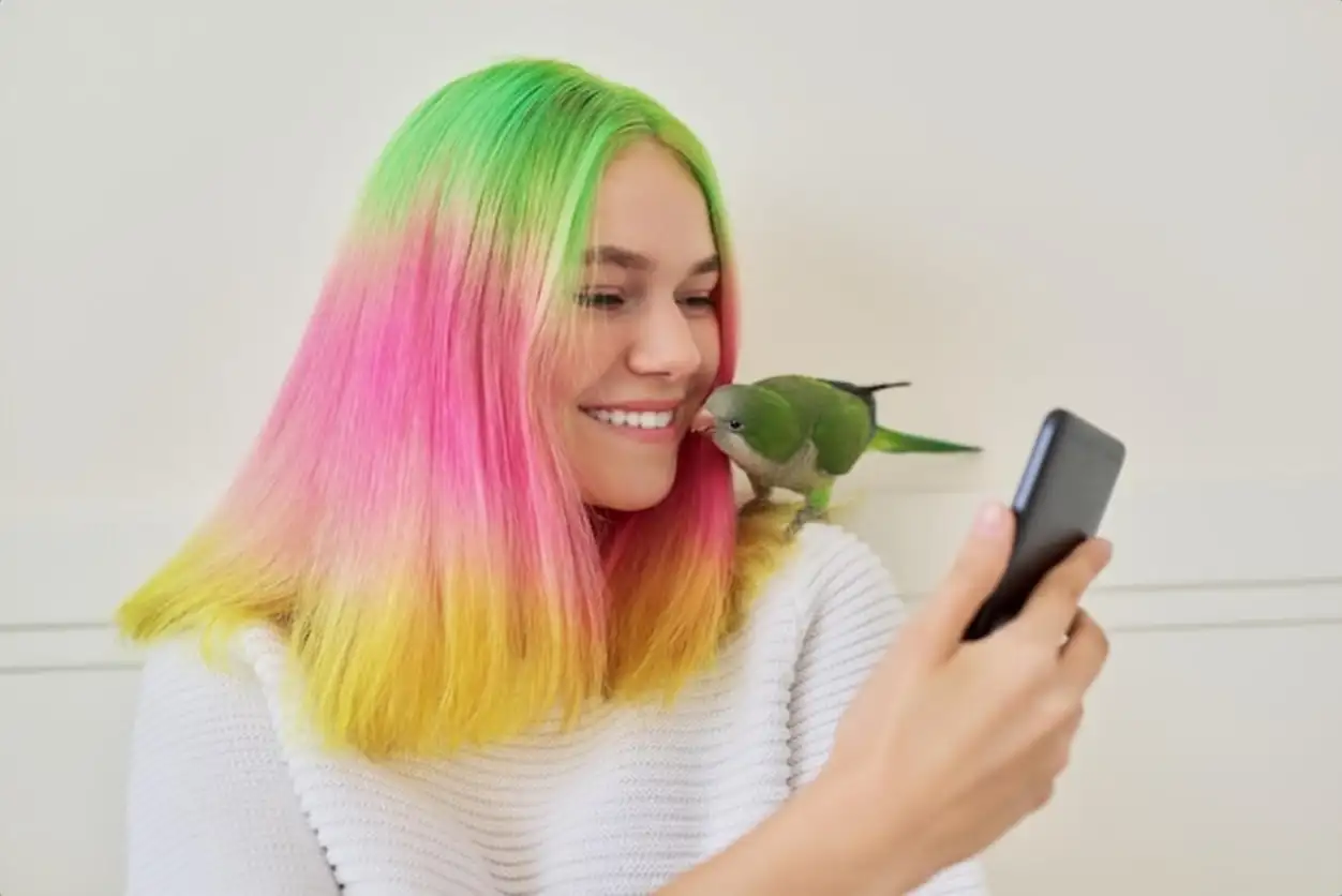 Trendy teen girl with smartphone and quaker parrot on her shoulder