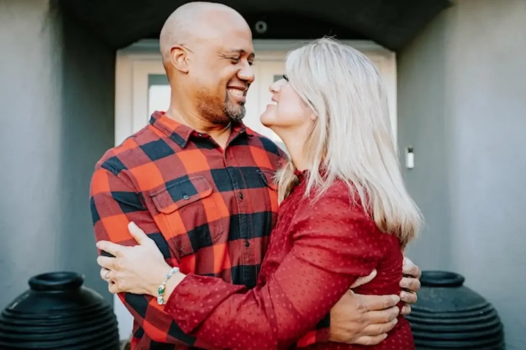 Mixed race couple embraces warmly smiling at each other They wear red plaid and red tops sharing a joyful moment The couple stands close enjoying each other39s company Mixed race couple hugging