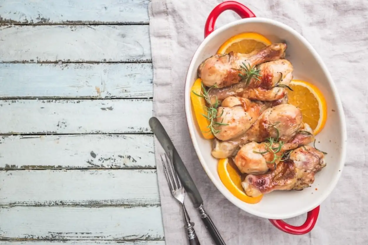 Baked chicken drumstick in a dish with orange and rosemary, top view