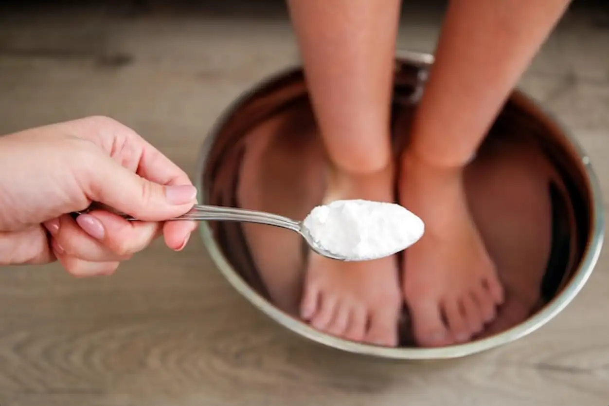 Foot baths in hot water A woman puts a spoonful of soda in the water