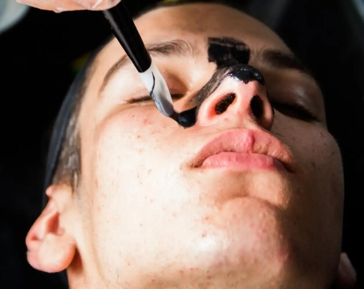 Cropped hand of beautician applying facial mask on teenage boy