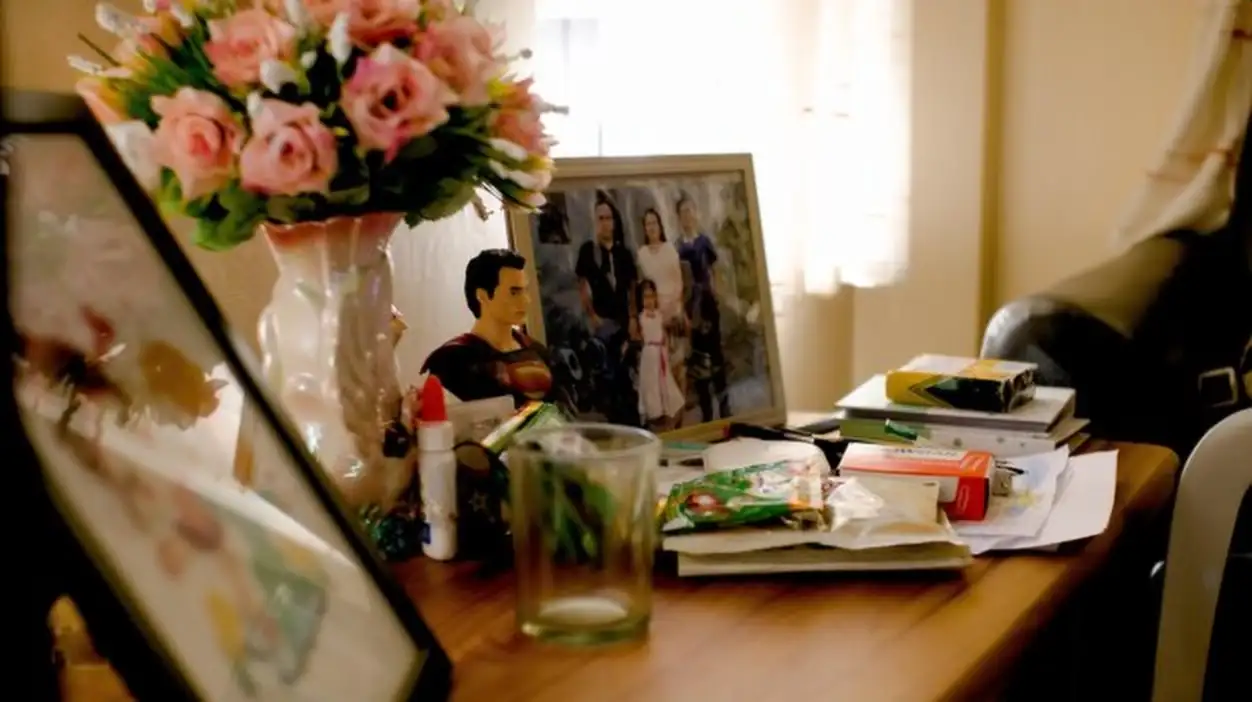 Frame with family photograph standing on wooden table among household items near bunch of flowers
