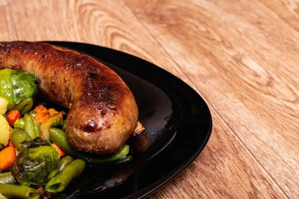 Grilled vegetables and sausage on a black plate