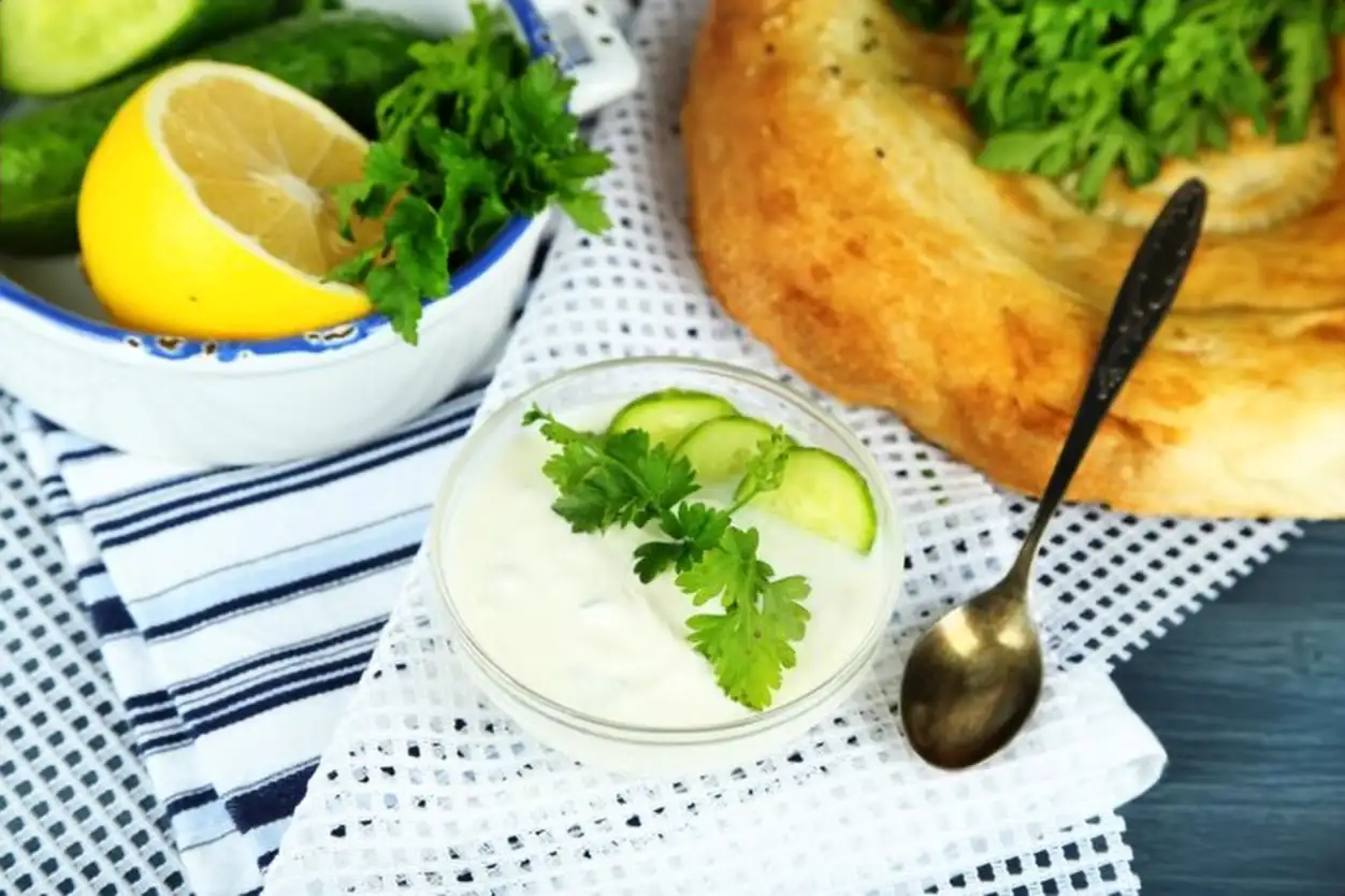 Cucumber yogurt in glass bowl and homemade bread on color napkin on wooden background