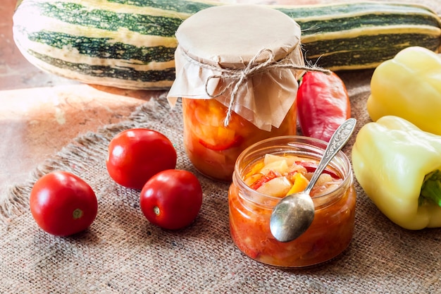 Homemade preserving. Zucchini and bell pepper salad in glass jar with ingredients on background
