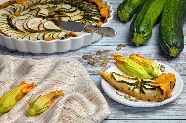 Slice of zucchini courgette and cheese pie on a white plate surrounded by flowers zucchini pie platter On a rough painted table Selective focus