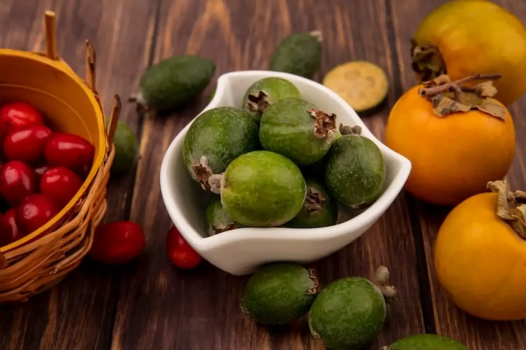 Top view of tasty sweet feijoas on a bowl with cornelian cherries on a bucket with persimmon fruits isolated on a wooden background