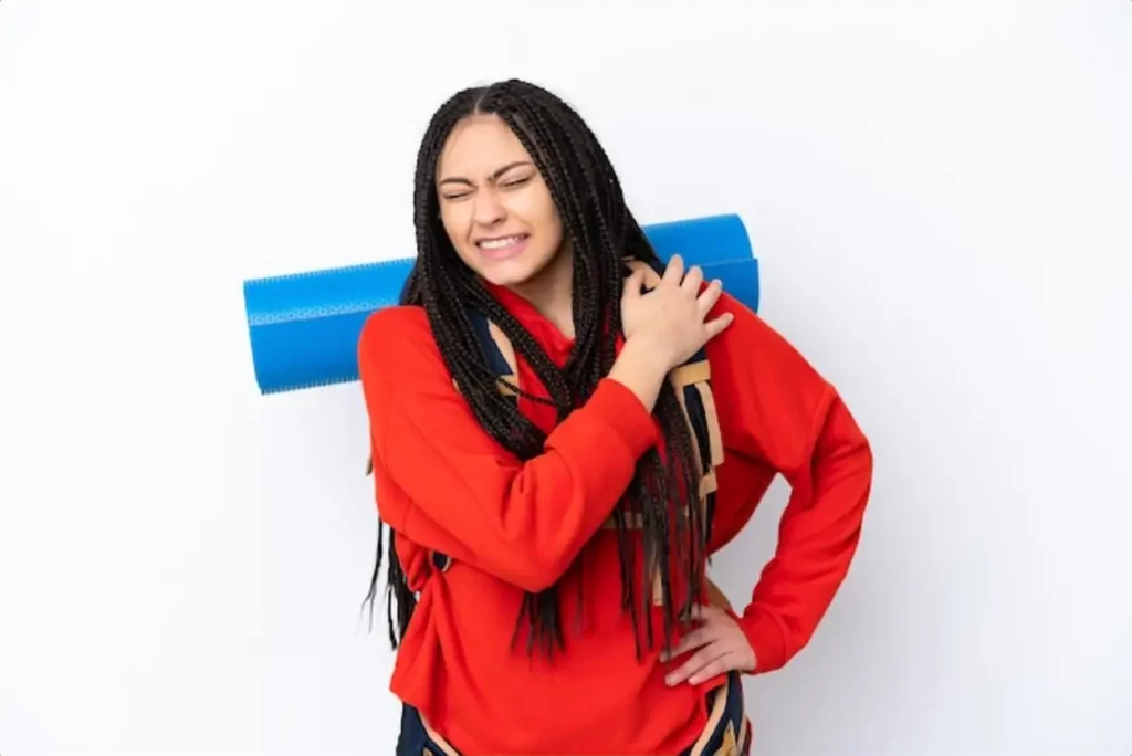 Hiker teenager girl with braids over isolated white background suffering from pain in shoulder for having made an effort