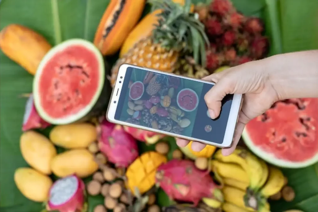 Woman hand take phone photography of tropical fruits. Sweet mango, papaya, pitahaya, banana, watermelon, pineapple. Raw vegan vegetarian healthy food, close up