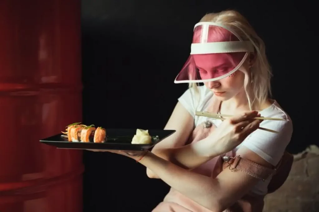 Plate of sushi rolls in restaurant with woman holding chopsticks