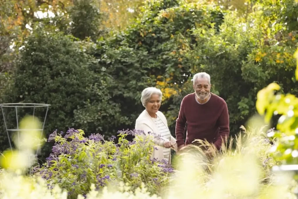 Happy senior biracial couple holding hands and looking at plants in garden at home copy space