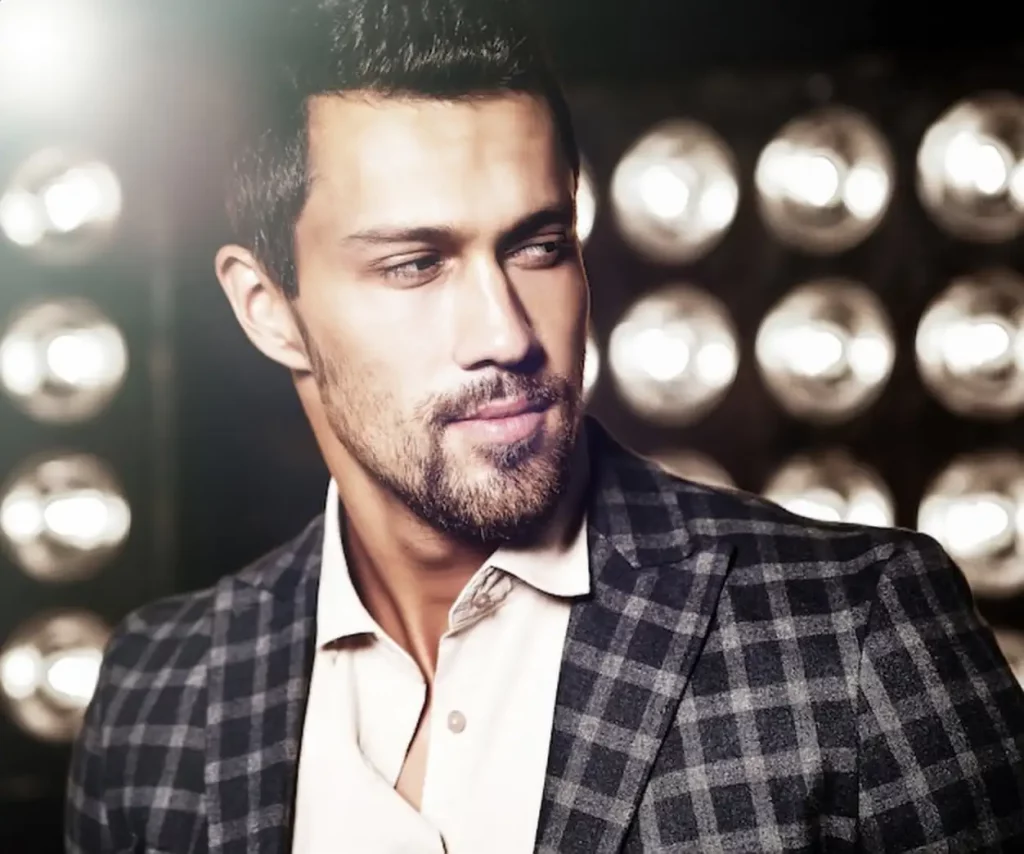 portrait of sexy handsome fashion male model man dressed in elegant suit on black studio lights background
