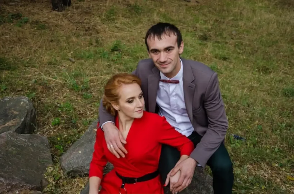 A girl in a red dress and a guy in a suit are sitting on a stone in the forest