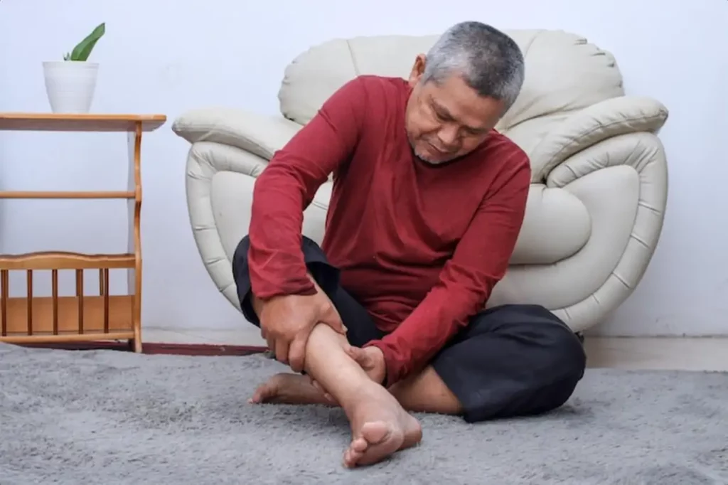 Senior man sitting on floor have cramps in his calves massage the calf by hands