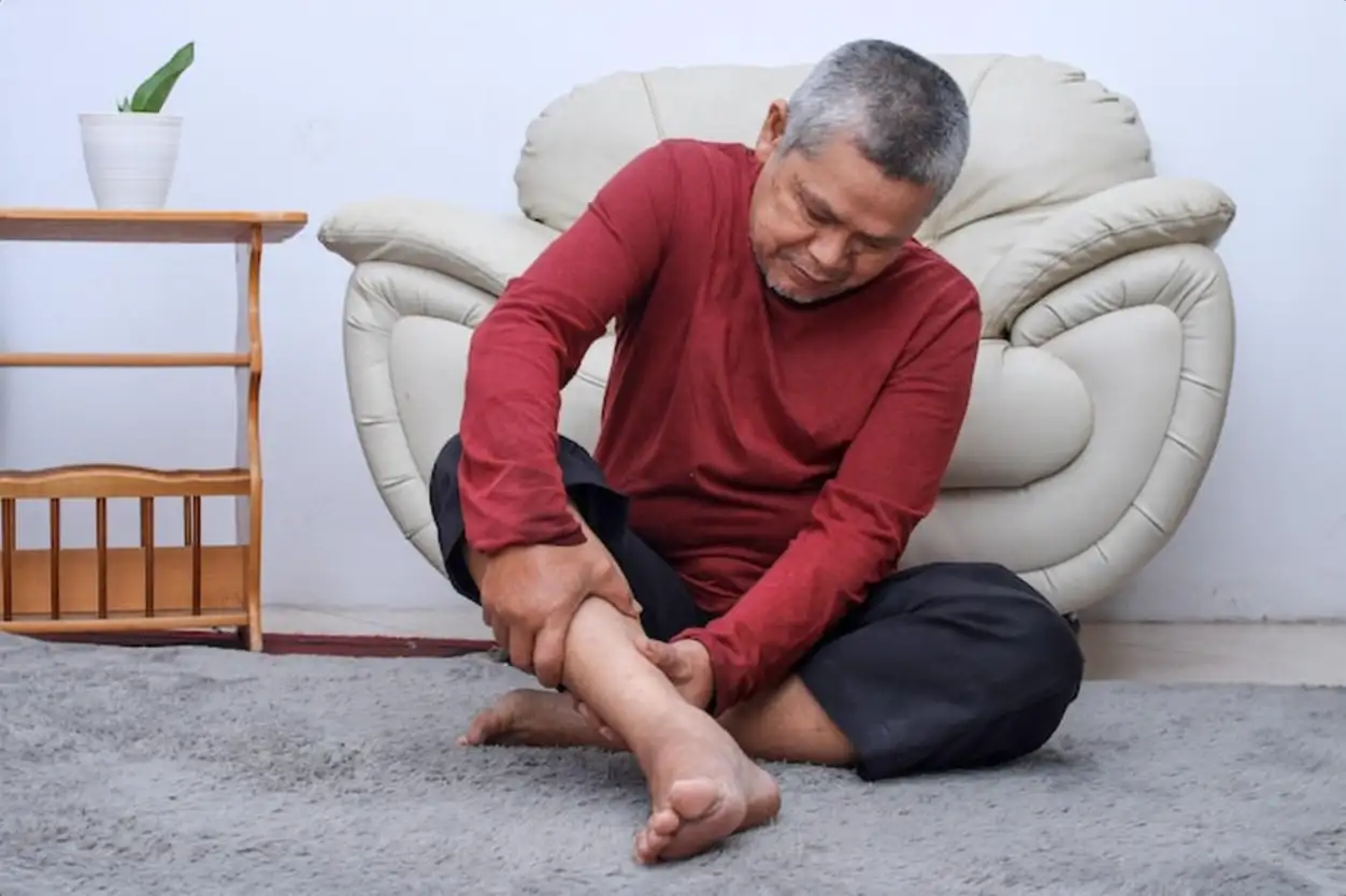 Senior man sitting on floor have cramps in his calves massage the calf by hands