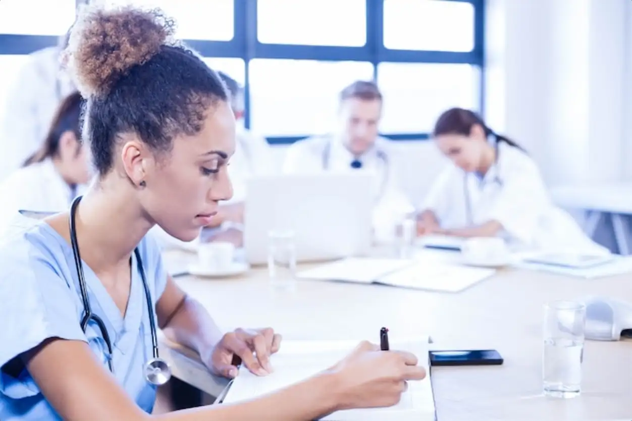 Female doctors writing on clipboard and other doctors discussing behind in conference room