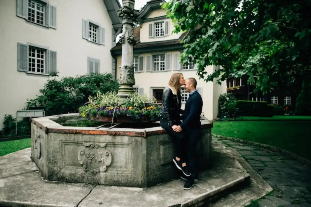 Love story. Young couple in love kissing near beautiful fountain with flowers.