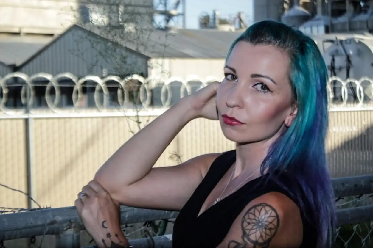 Portrait of young woman with green dyed hair while standing by fence