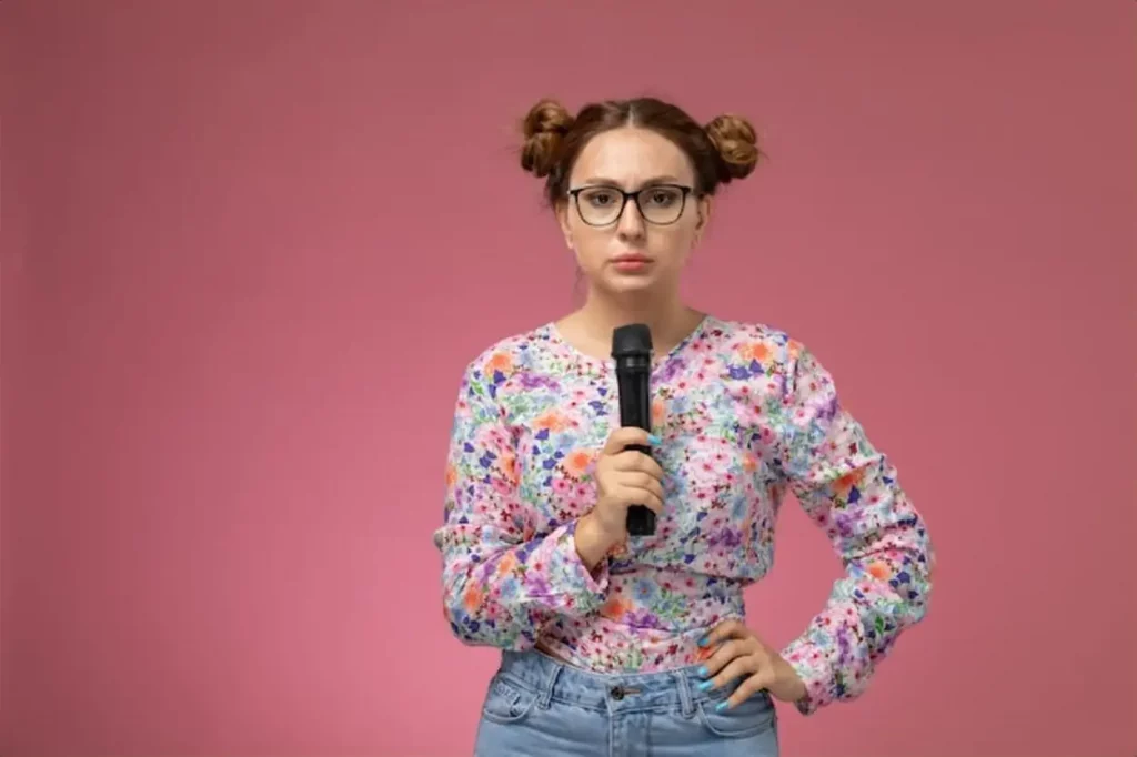 Front view young female in flower designed shirt trying to sign wiht microphone the pink background