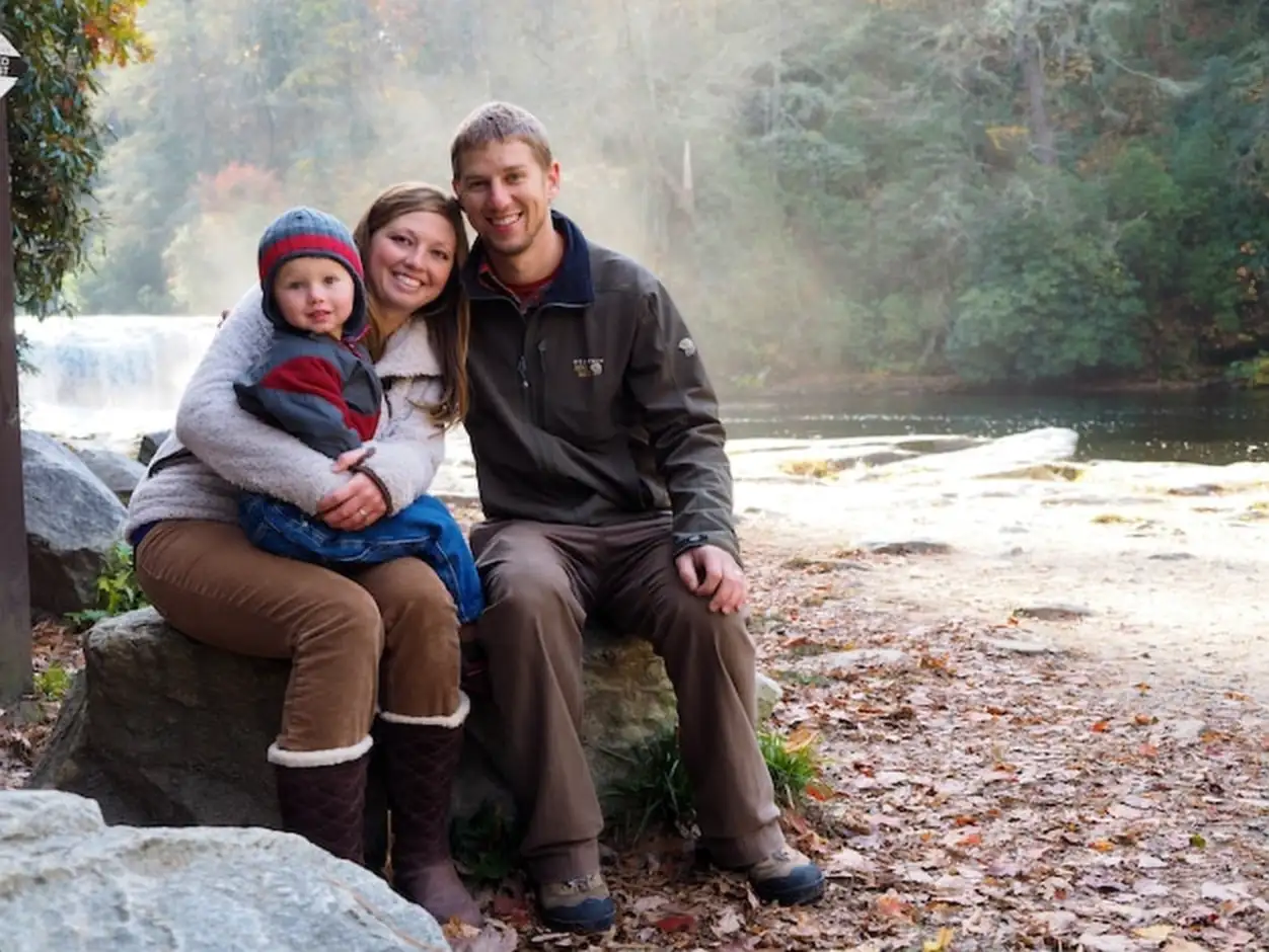 Family sitting on a rock surrounded by a waterfall and greenery under the sunlight